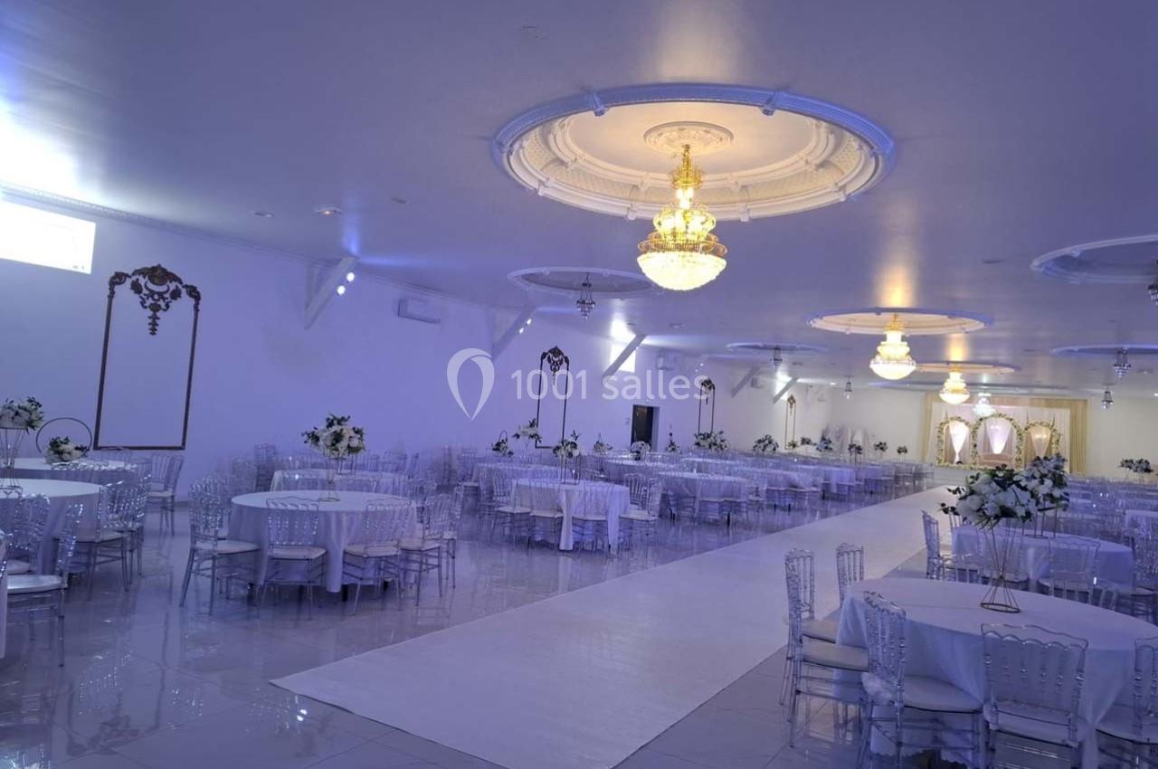Salle de réception élégante avec tables rondes décorées de fleurs blanches et lustres suspendus au plafond.