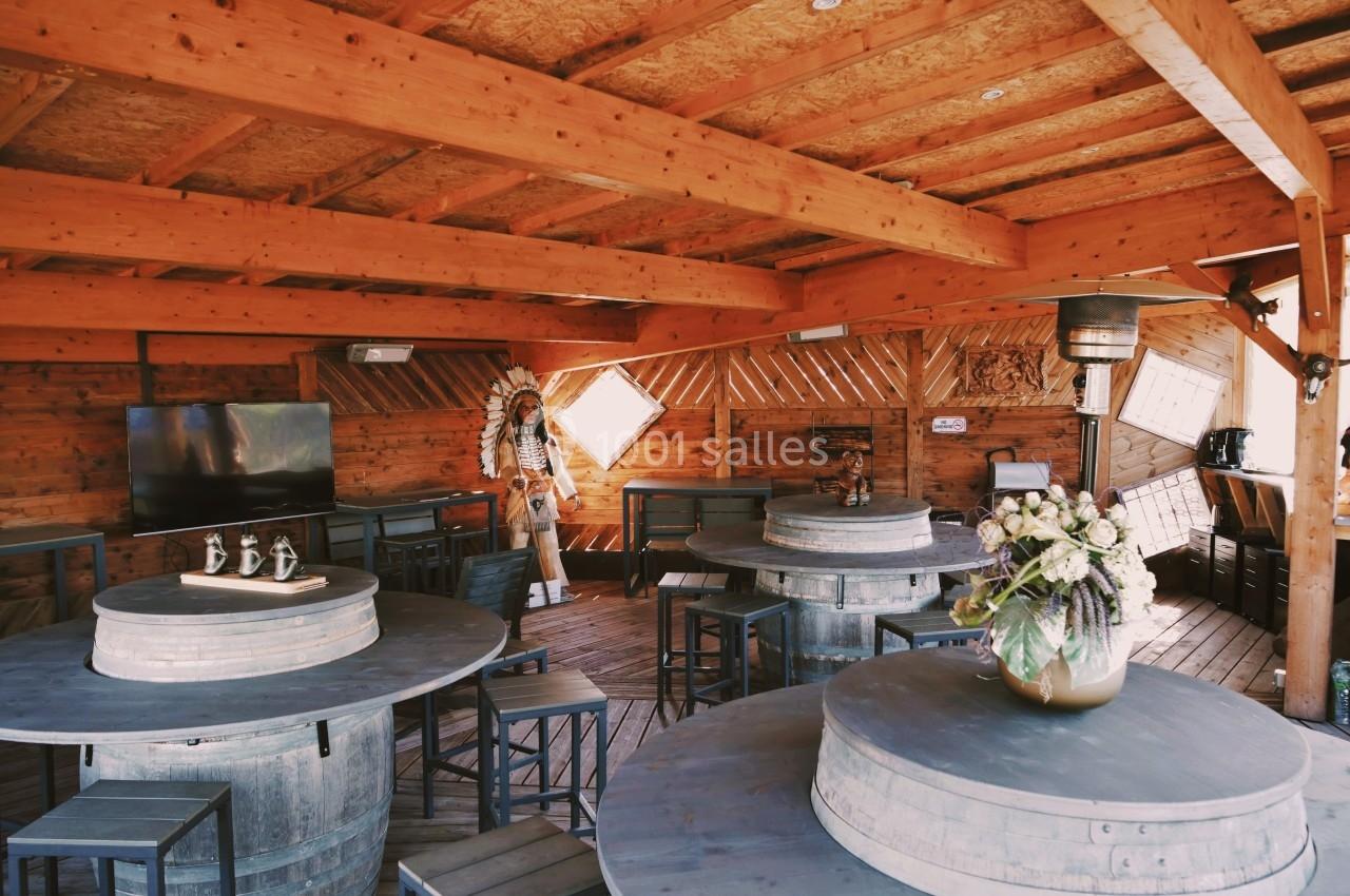 Intérieur d'une terrasse en bois avec tables rondes sur des tonneaux, chaises et décoration rustique.