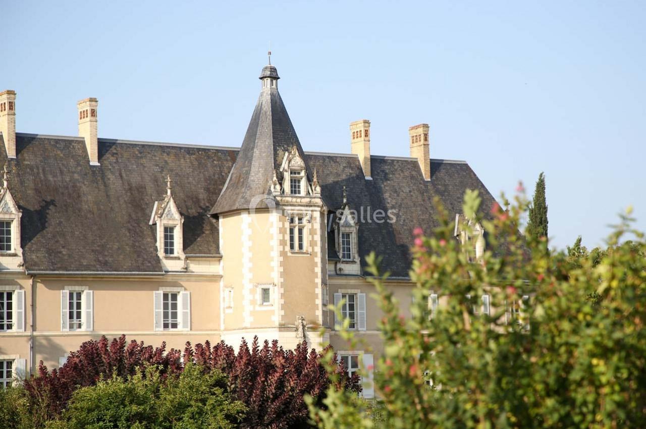 Façade d'un château avec une tour centrale, entouré de végétation sous un ciel dégagé.