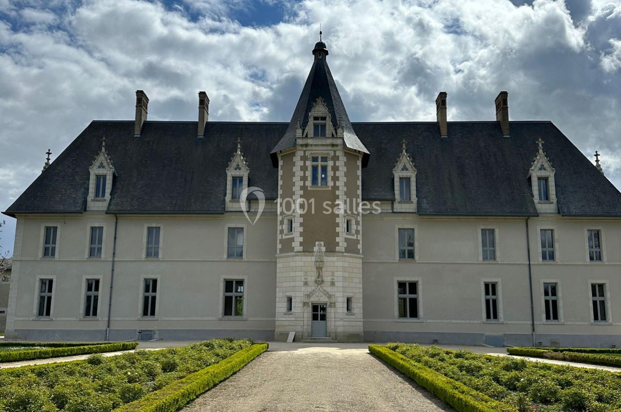 Façade d'un château avec une tour centrale, entouré de jardins symétriques sous un ciel partiellement nuageux.