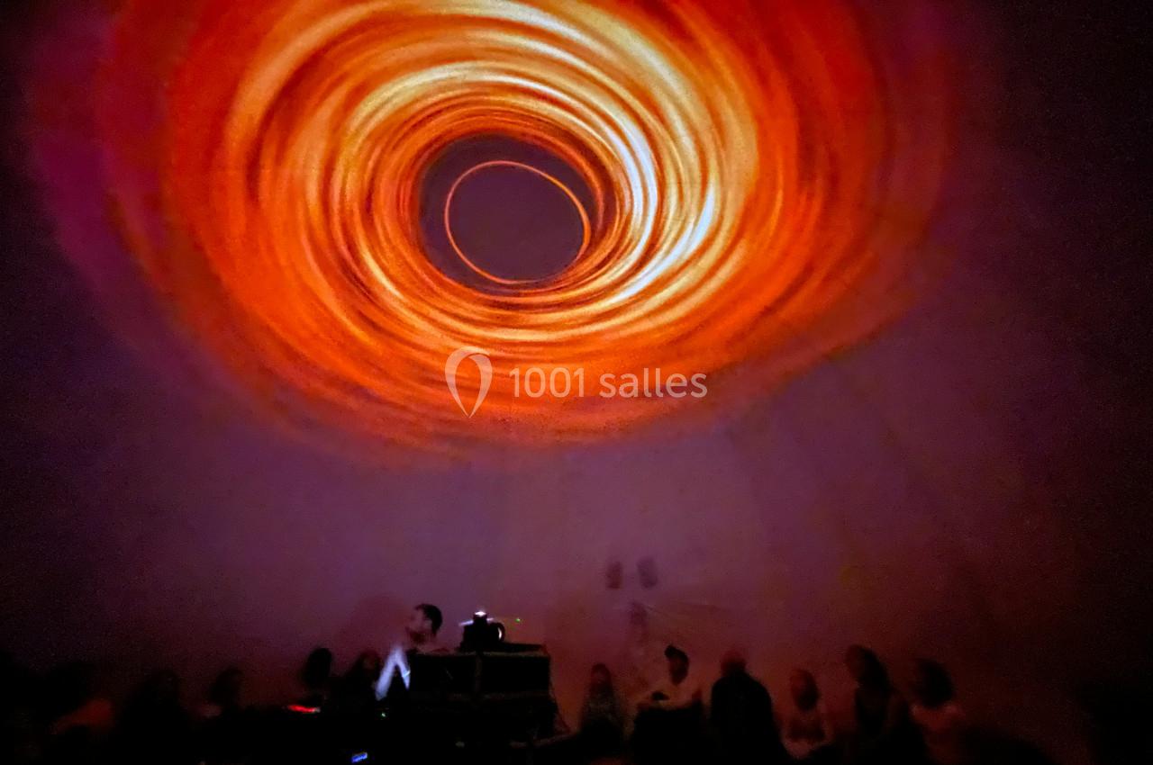 Projection lumineuse en spirale orange sur un plafond, avec des silhouettes de spectateurs assis en contrebas.