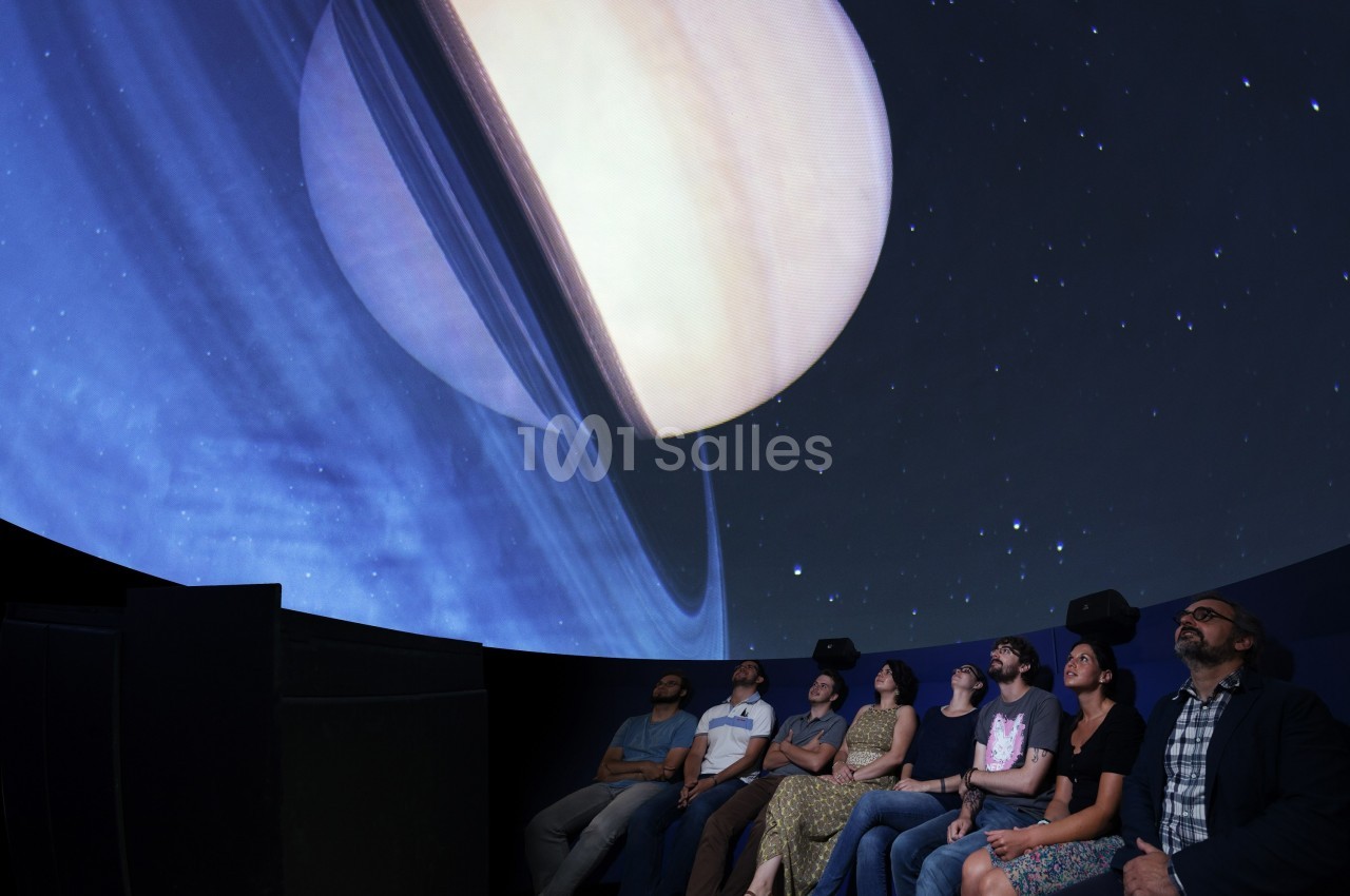 Des personnes assises dans un planétarium regardent une projection immersive de Saturne et de ses anneaux.