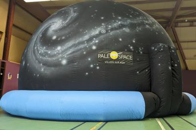 Dôme gonflable noir avec motif de galaxie, utilisé pour des projections, installé dans un gymnase.