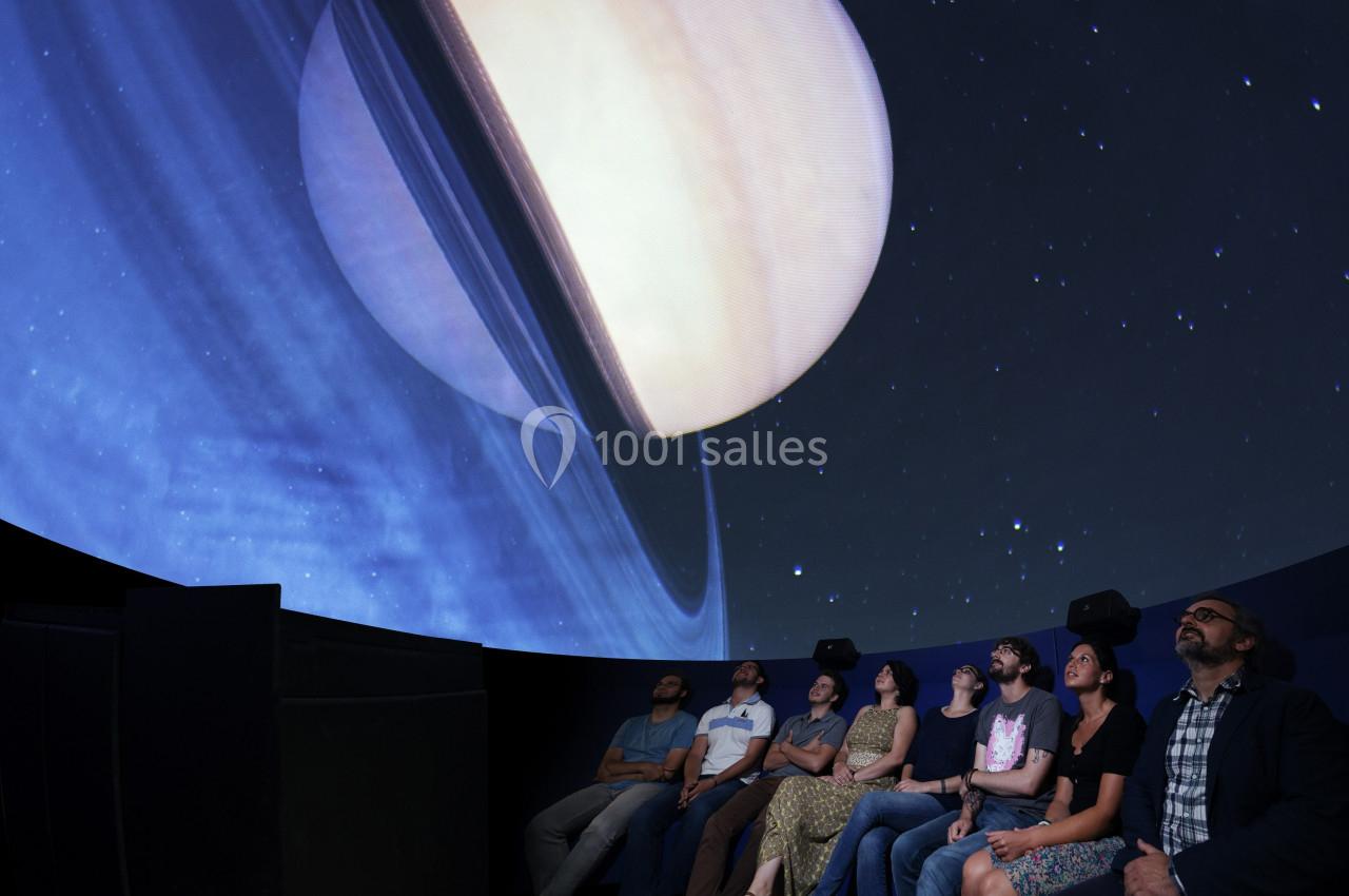 Des personnes assises dans un planétarium regardent une projection immersive de Saturne et de ses anneaux.