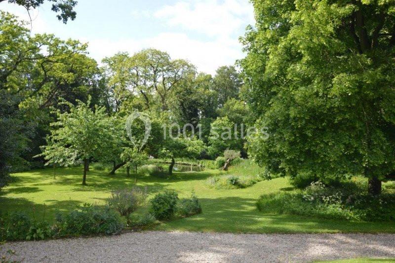 Jardin verdoyant avec pelouse, arbres feuillus, buissons et un petit étang sous un ciel partiellement dégagé.