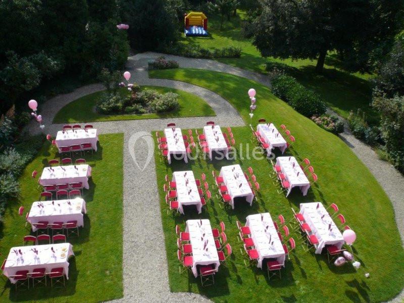 Tables dressées avec nappes roses et chaises rouges disposées dans un jardin pour un événement en plein air.