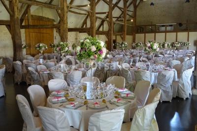 Bâtiment en pierre avec toit en pente, tables et chaises disposées sur une terrasse et une pelouse au premier plan.