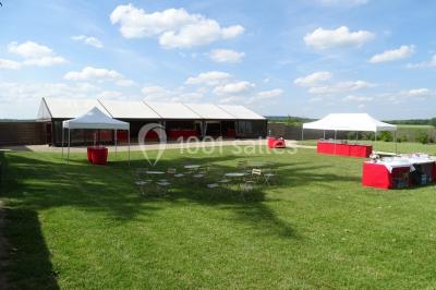 Bâtiment en pierre avec toit en pente, tables et chaises disposées sur une terrasse et une pelouse au premier plan.