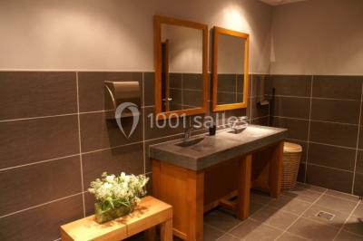 Bâtiment en pierre avec toit en pente, tables et chaises disposées sur une terrasse et une pelouse au premier plan.