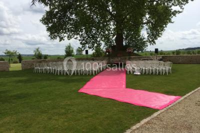 Bâtiment en pierre avec toit en pente, tables et chaises disposées sur une terrasse et une pelouse au premier plan.