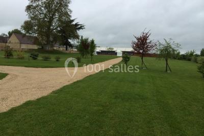 Bâtiment en pierre avec toit en pente, tables et chaises disposées sur une terrasse et une pelouse au premier plan.