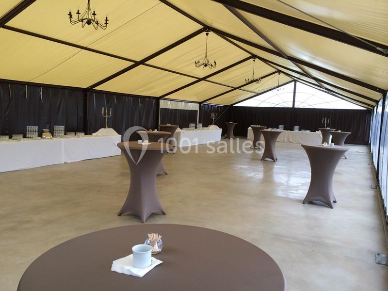 Intérieur d'une tente de réception avec tables hautes nappées de brun et buffets alignés le long des parois.