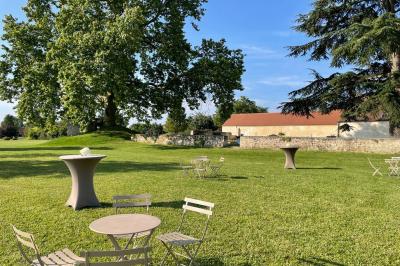 Bâtiment en pierre avec toit en pente, tables et chaises disposées sur une terrasse et une pelouse au premier plan.