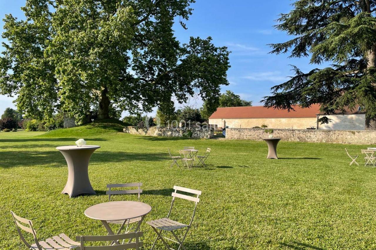 Chaises et tables disposées sur une pelouse verdoyante, entourées d'arbres et d'un bâtiment en arrière-plan.