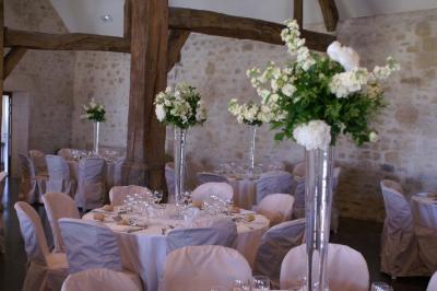 Bâtiment en pierre avec toit en pente, tables et chaises disposées sur une terrasse et une pelouse au premier plan.