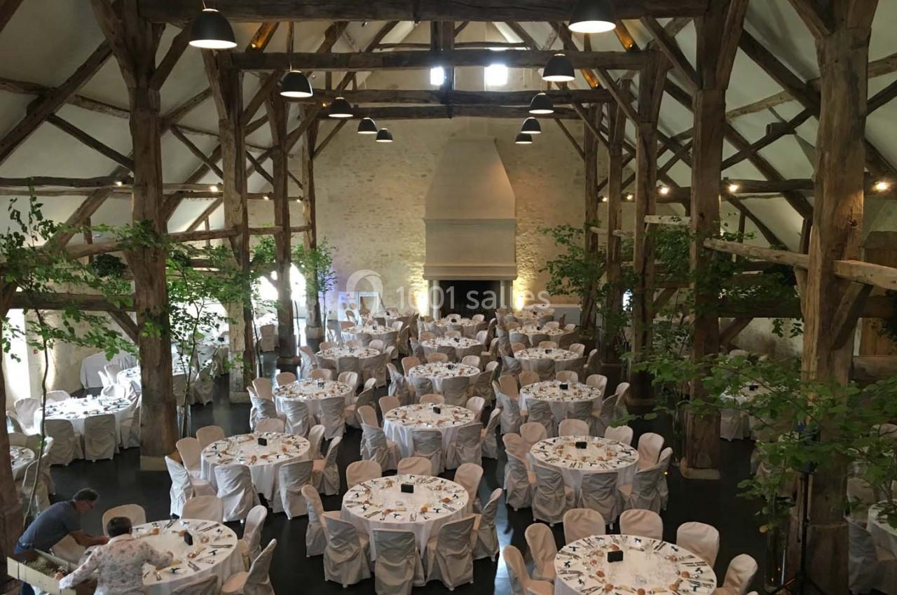 Salle de réception avec charpente en bois, tables rondes dressées et décorations végétales.