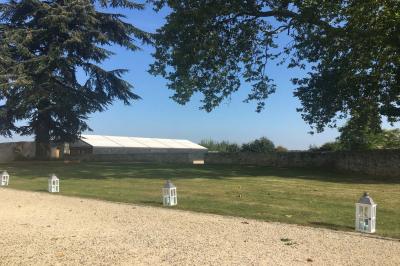 Bâtiment en pierre avec toit en pente, tables et chaises disposées sur une terrasse et une pelouse au premier plan.