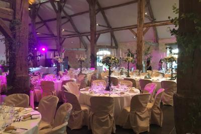 Bâtiment en pierre avec toit en pente, tables et chaises disposées sur une terrasse et une pelouse au premier plan.