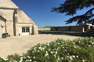Bâtiment en pierre avec toit en pente, tables et chaises disposées sur une terrasse et une pelouse au premier plan.