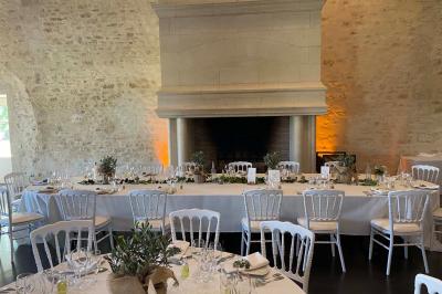 Bâtiment en pierre avec toit en pente, tables et chaises disposées sur une terrasse et une pelouse au premier plan.