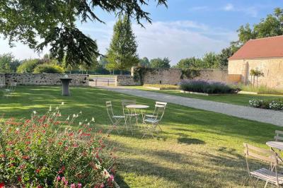 Bâtiment en pierre avec toit en pente, tables et chaises disposées sur une terrasse et une pelouse au premier plan.
