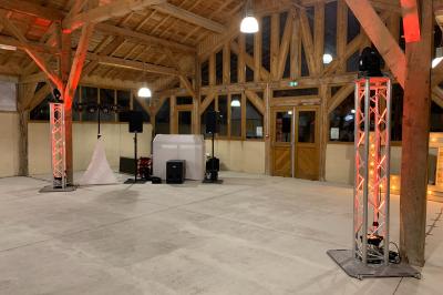 Grande salle en bois avec charpente apparente, éclairages rouges, matériel de sonorisation et espace vide au centre.