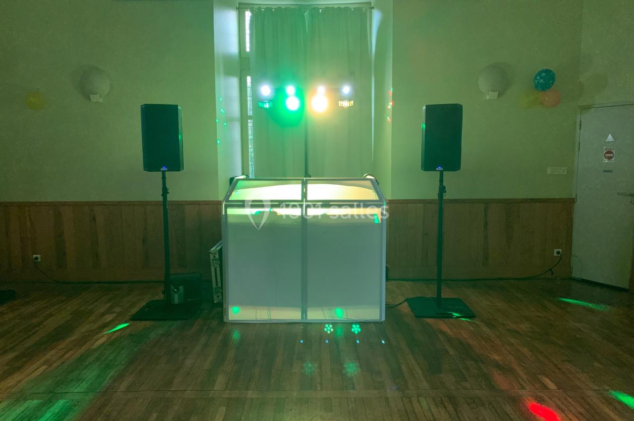 Console de DJ éclairée avec des lumières colorées, entourée de deux enceintes dans une salle aux murs en bois.