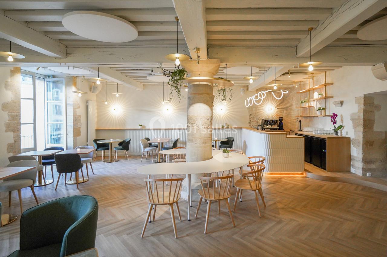 Salle lumineuse avec mobilier moderne, poutres apparentes, parquet en bois clair et un comptoir avec éclairage intégré.