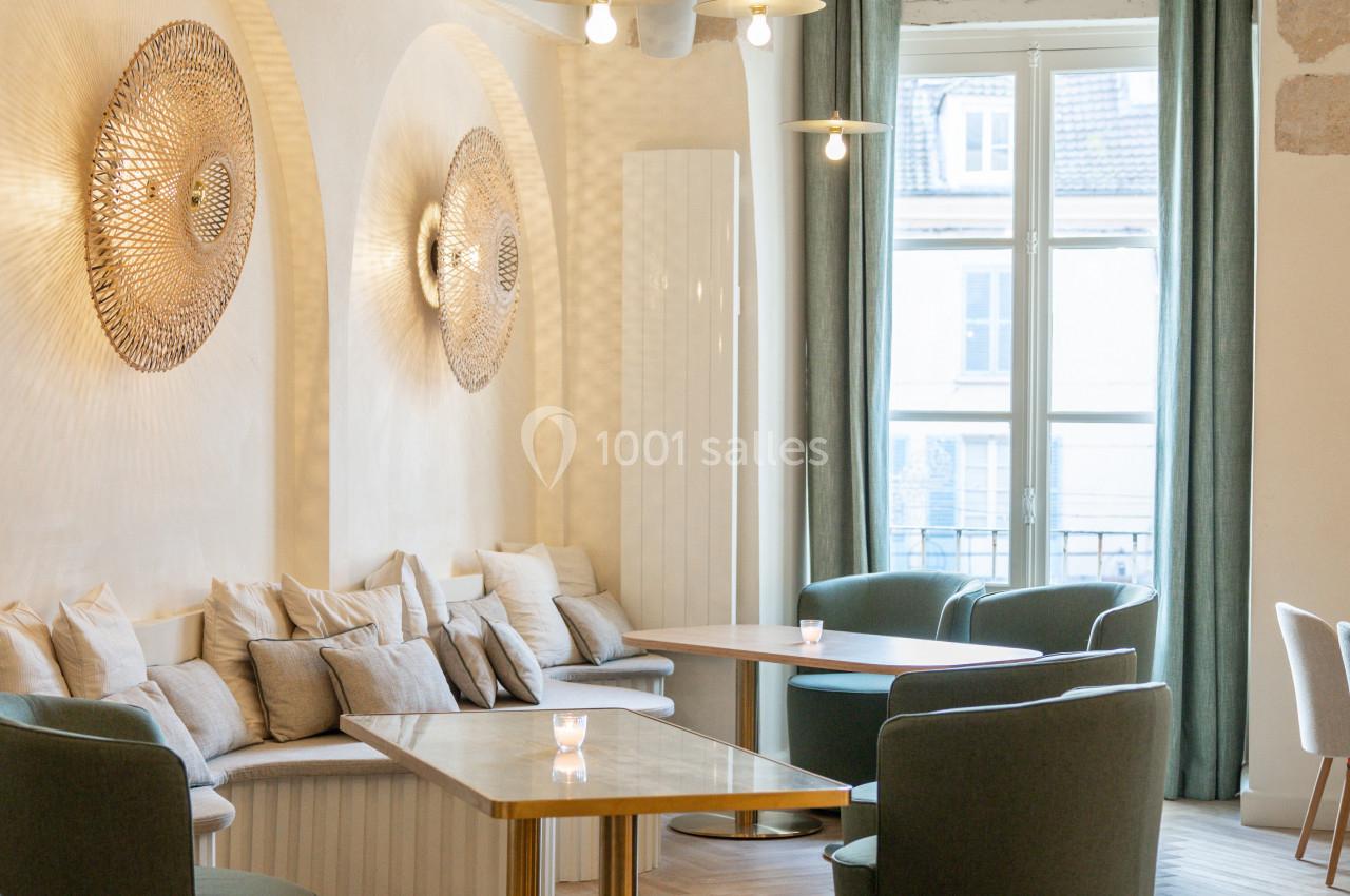 Espace lumineux avec tables, fauteuils verts, banquettes et décorations murales dans un intérieur moderne et épuré.