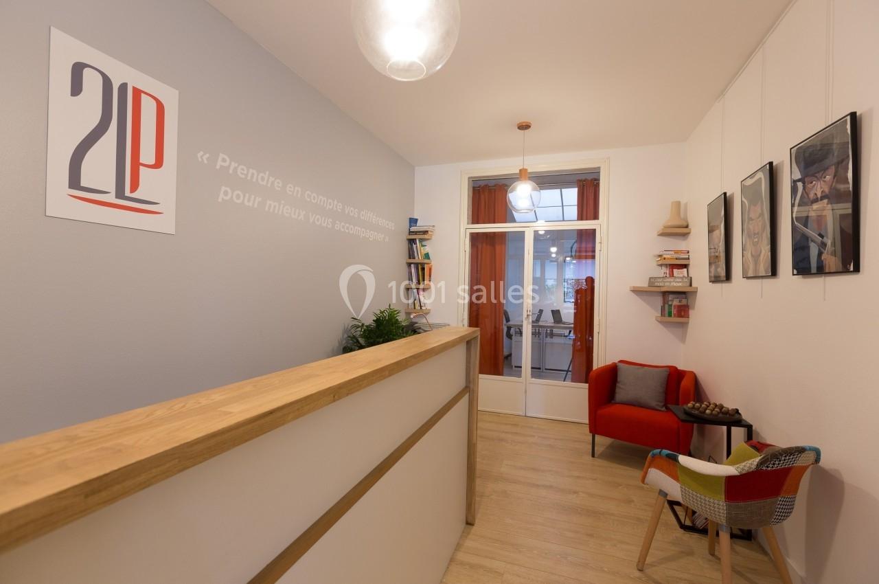 Intérieur d'un bureau avec un comptoir en bois, fauteuils colorés, étagères et affiches décoratives sur les murs.