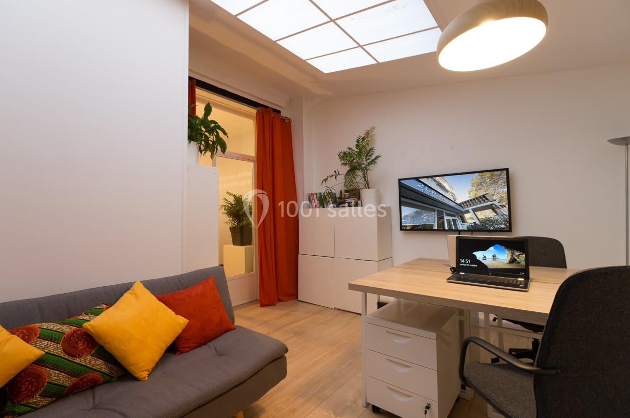 Bureau moderne avec canapé, table de travail, étagères, plantes et écran affichant une image architecturale.