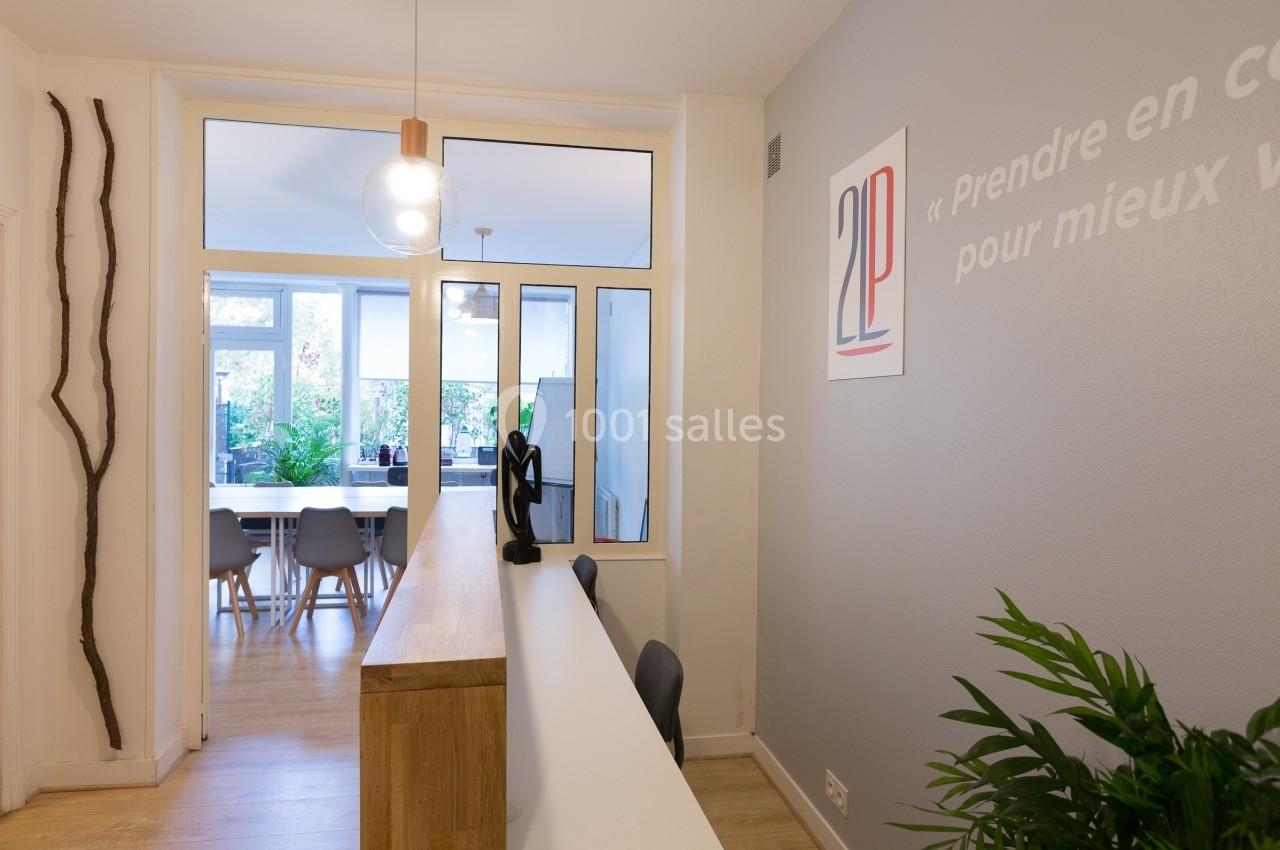 Bureau moderne avec comptoir d'accueil, plantes vertes et salle de réunion lumineuse en arrière-plan.