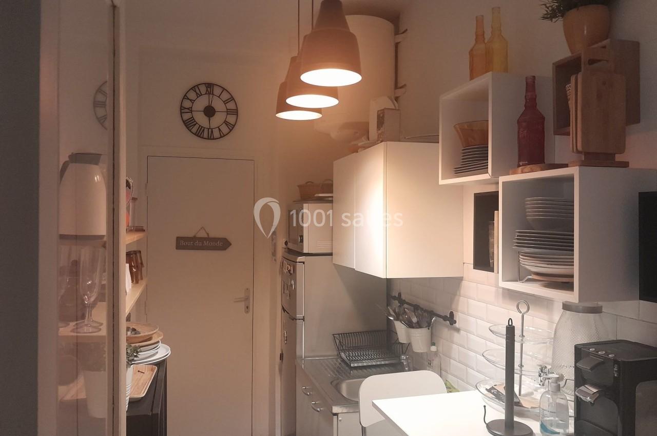 Cuisine étroite avec éclairage suspendu, étagères ouvertes, vaisselle visible et décoration murale.