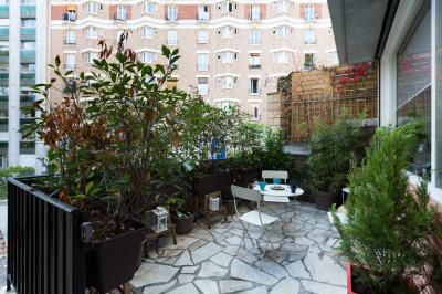 Terrasse en pierre avec mobilier de jardin, entourée de plantes en pots, donnant sur des immeubles en briques.