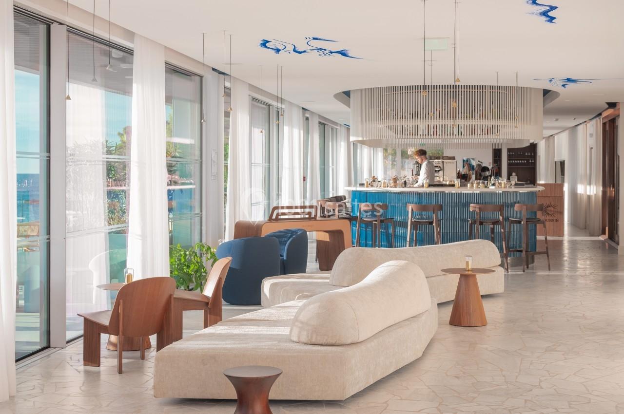 Espace lumineux avec mobilier moderne, canapés et bar central, grandes baies vitrées donnant sur l'extérieur.