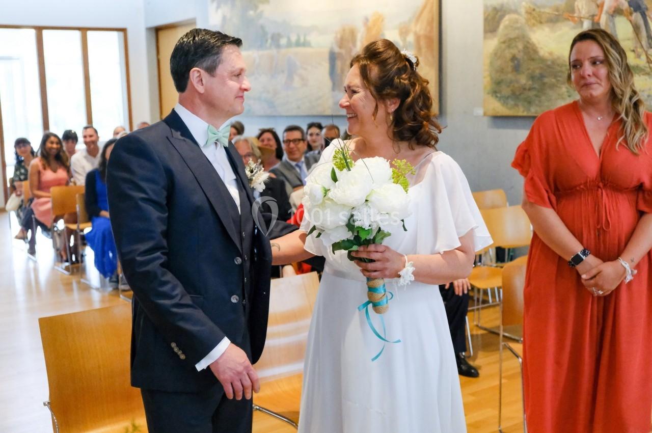 Un couple se regarde avec émotion lors d'une cérémonie de mariage, entouré d'invités assis dans une salle lumineuse.