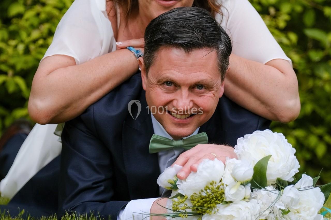 Un couple souriant allongé sur l'herbe, la femme posant ses mains sur les épaules de l'homme, avec un bouquet de fleurs…