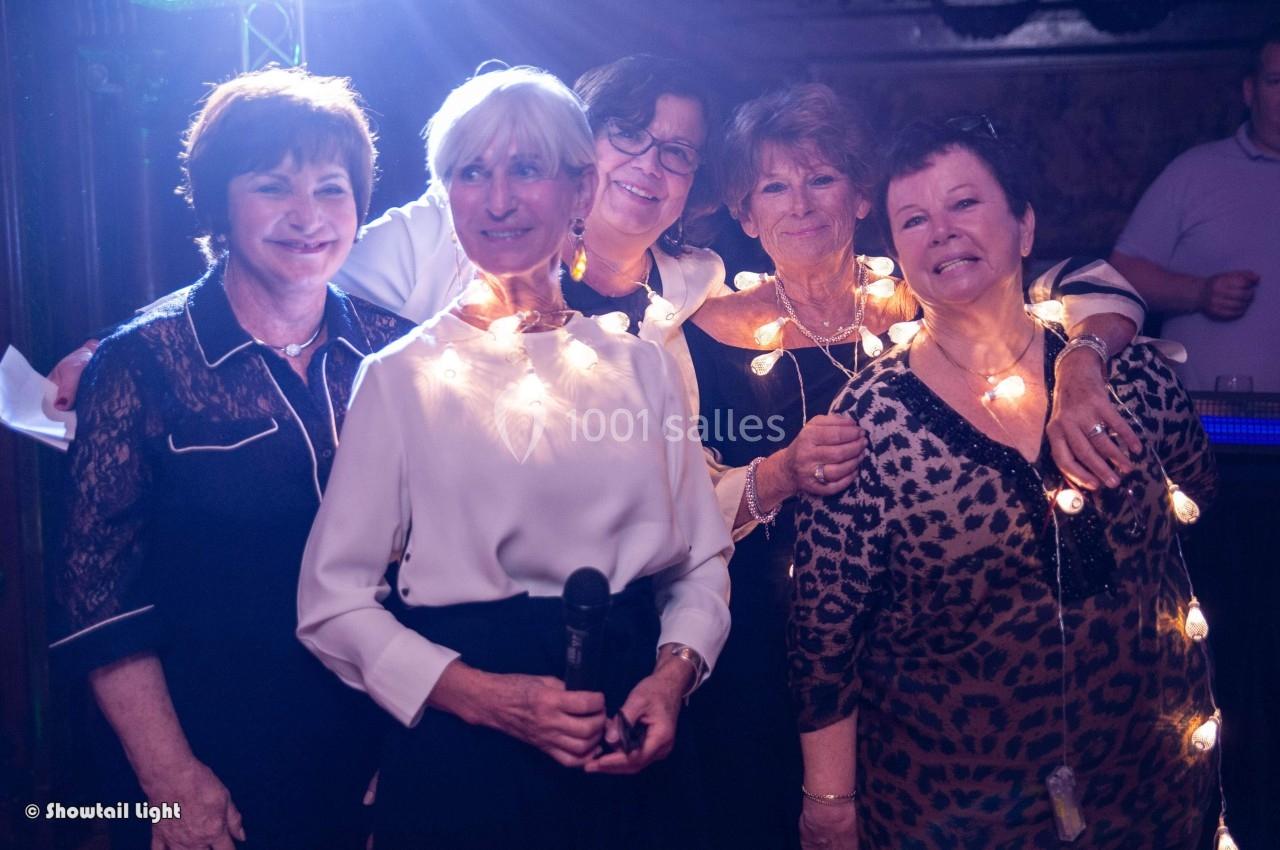 Cinq femmes souriantes posent ensemble, certaines portant des guirlandes lumineuses autour du cou.