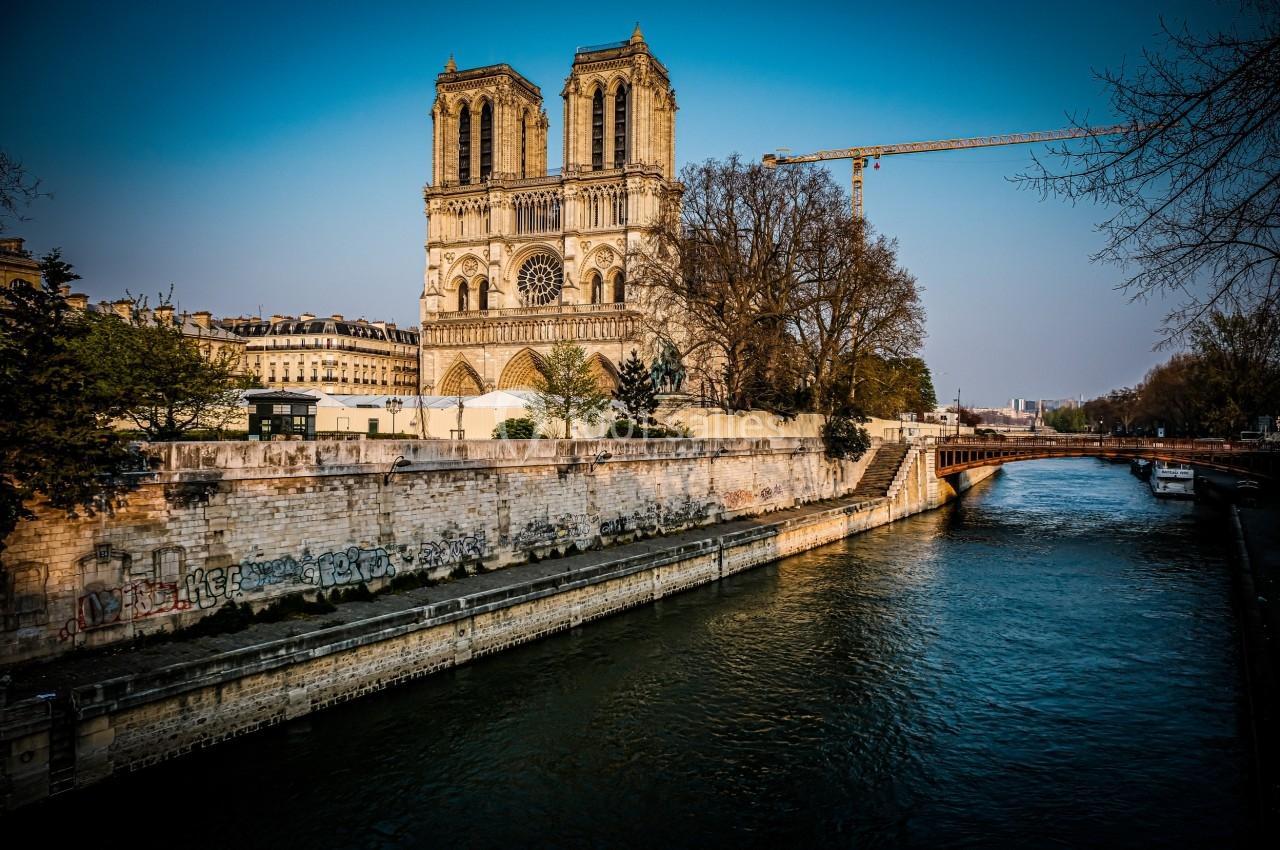 Vue de la cathédrale Notre-Dame de Paris depuis la Seine, avec un pont et une grue en arrière-plan.