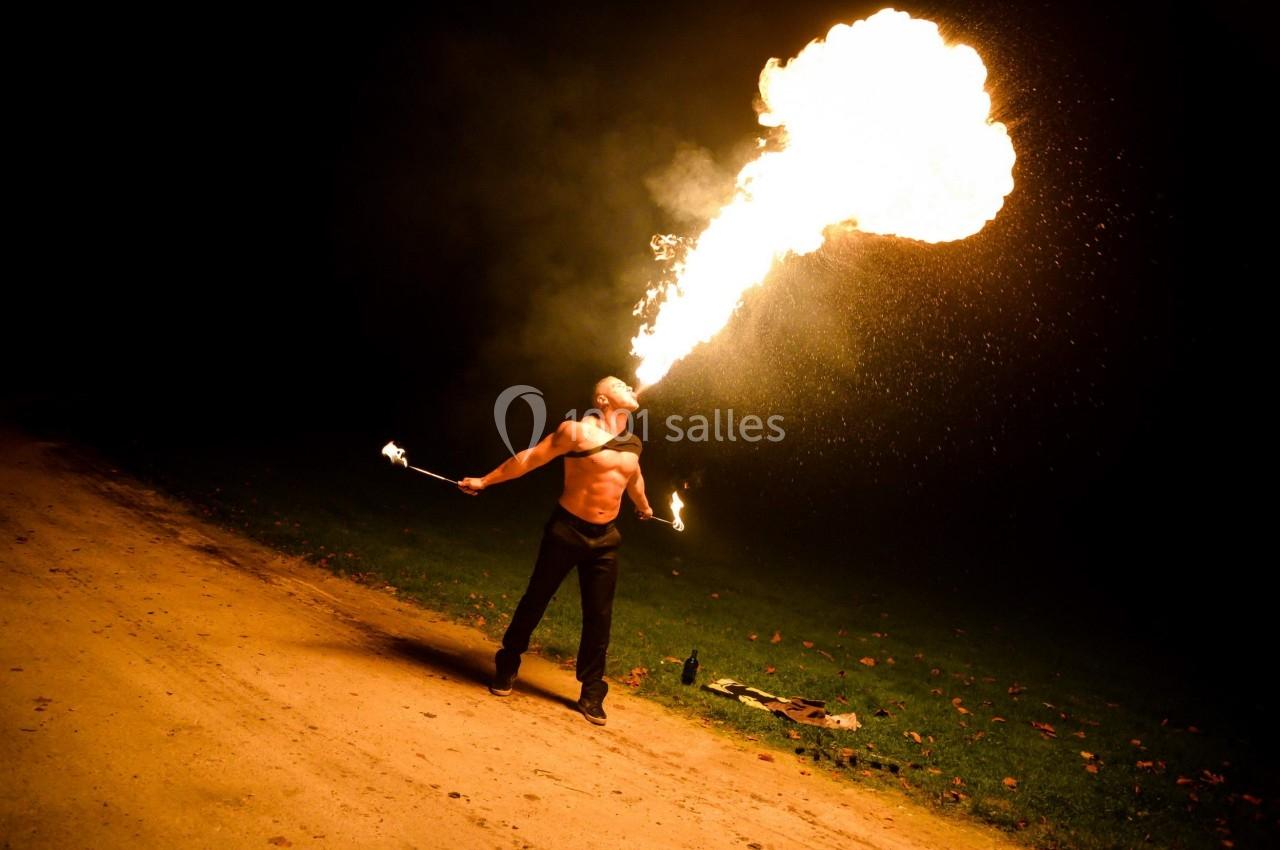 Un homme crache une grande flamme dans l'obscurité, tenant des torches enflammées dans chaque main.