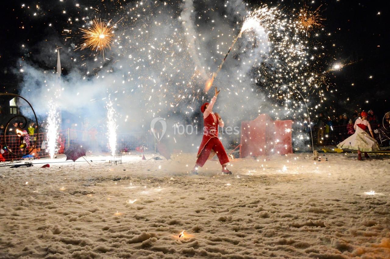 Un artiste en costume rouge manipule des bâtons enflammés dans un spectacle nocturne sur un sol enneigé.