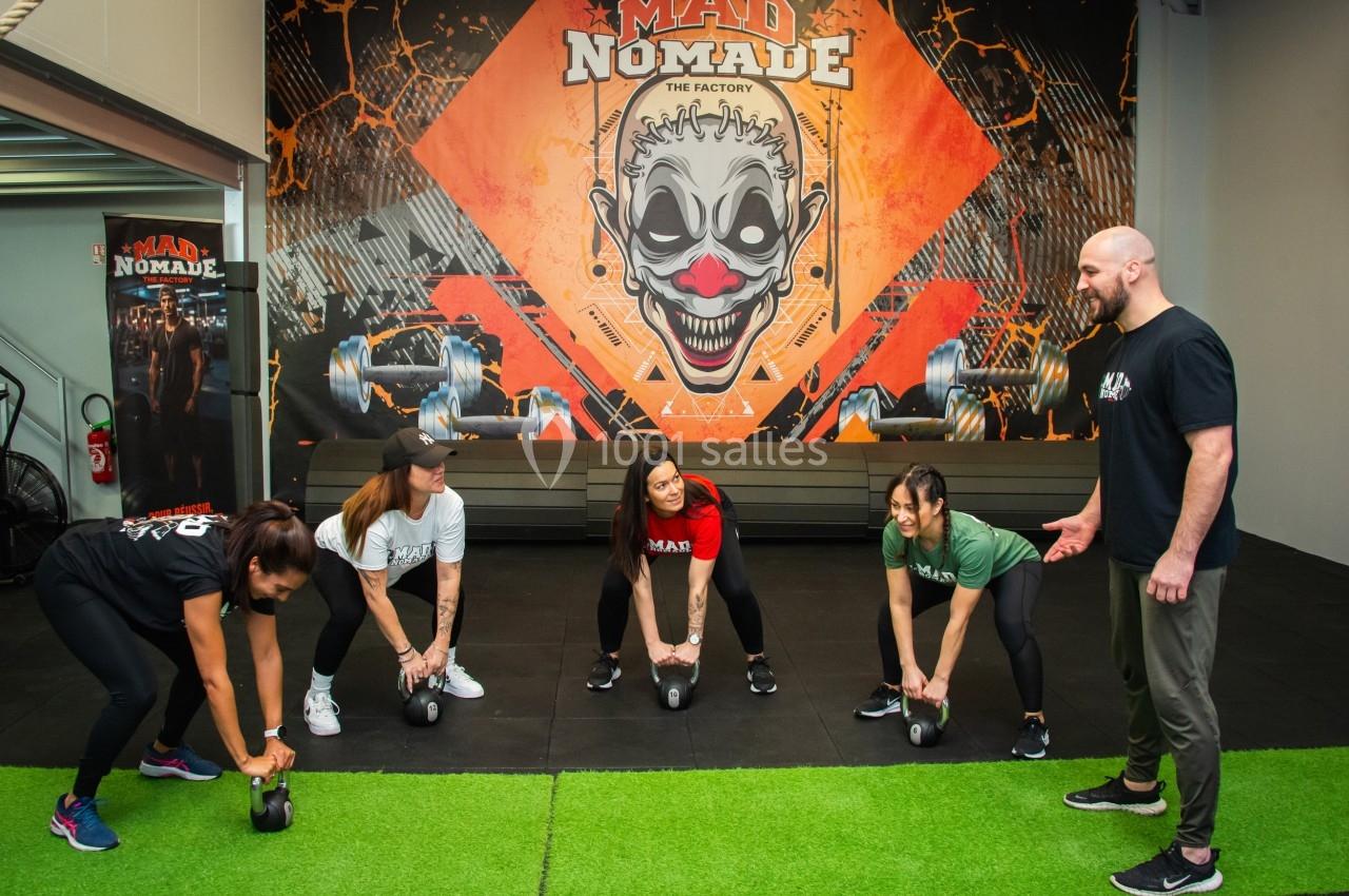 Quatre personnes s'entraînent avec des kettlebells sous la supervision d'un coach dans une salle de sport colorée.