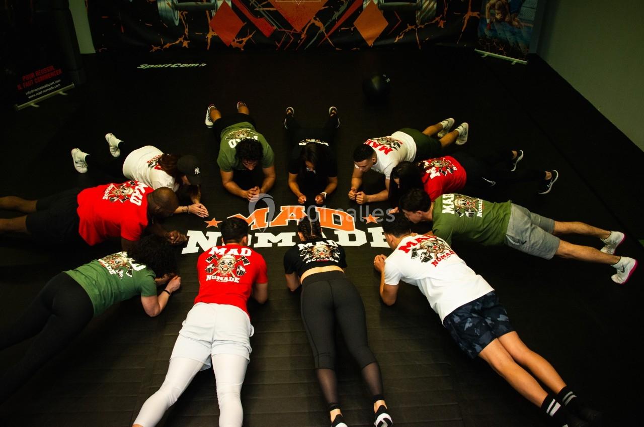 Un groupe de personnes en position de planche sur un sol noir, alignées autour d'un logo ’MAD NOMAD’.