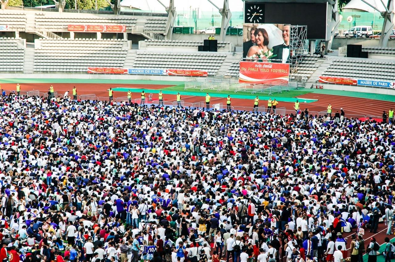 Foule rassemblée dans un stade avec une grande affiche publicitaire visible en arrière-plan.