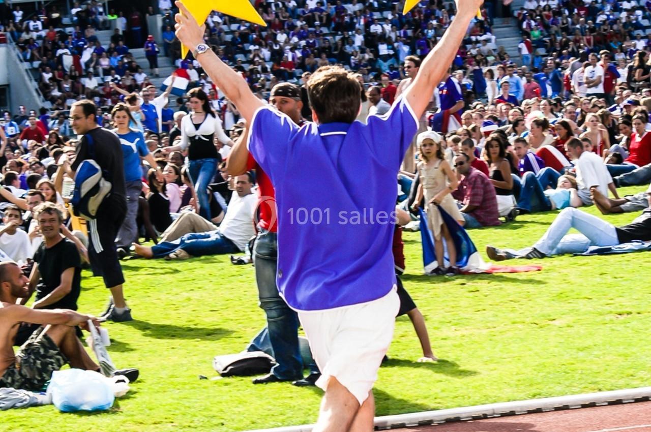 Un homme en tenue sportive court sur une piste, tenant deux étoiles jaunes, devant une foule assise dans un stade.