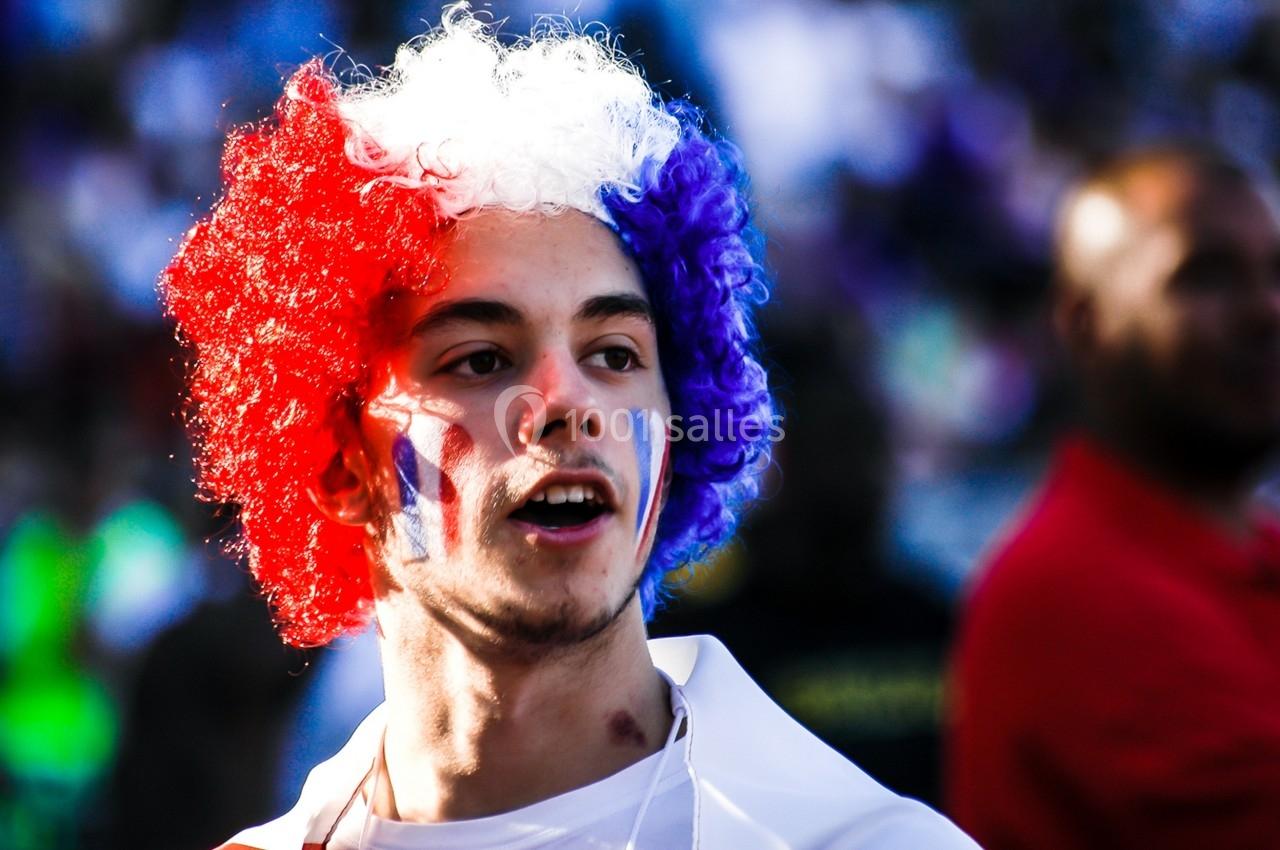 Un homme portant une perruque tricolore et des peintures faciales aux couleurs de la France dans une foule.