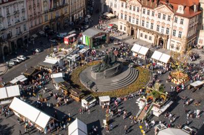Vue aérienne d'une place animée avec des stands, une statue centrale et des bâtiments historiques environnants.