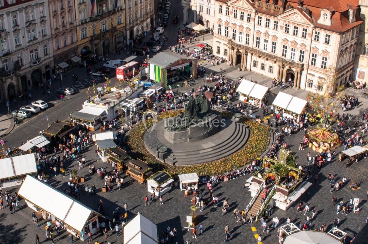 Vue aérienne d'une place animée avec des stands, une statue centrale et des bâtiments historiques environnants.