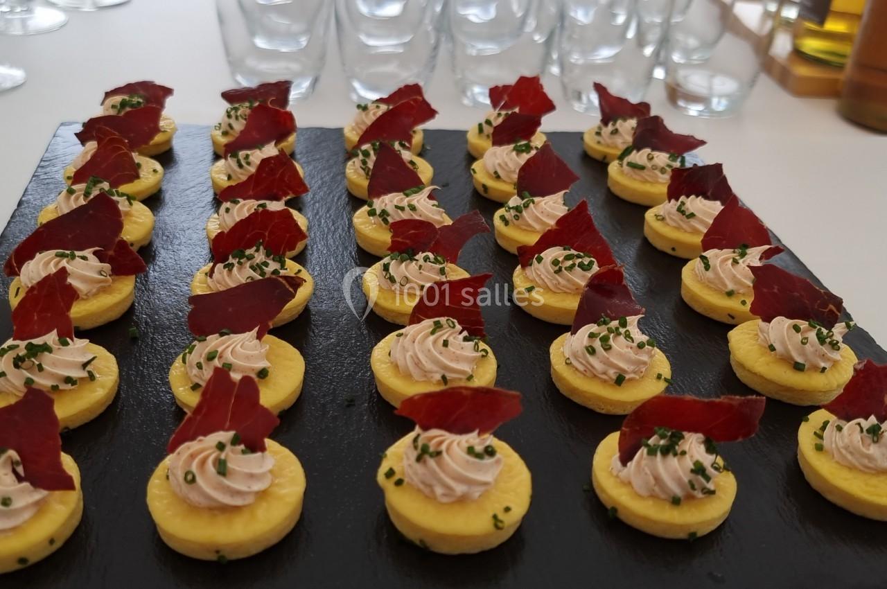 Plateau de bouchées apéritives sur ardoise, garnies de mousse et décorées de morceaux de viande séchée.
