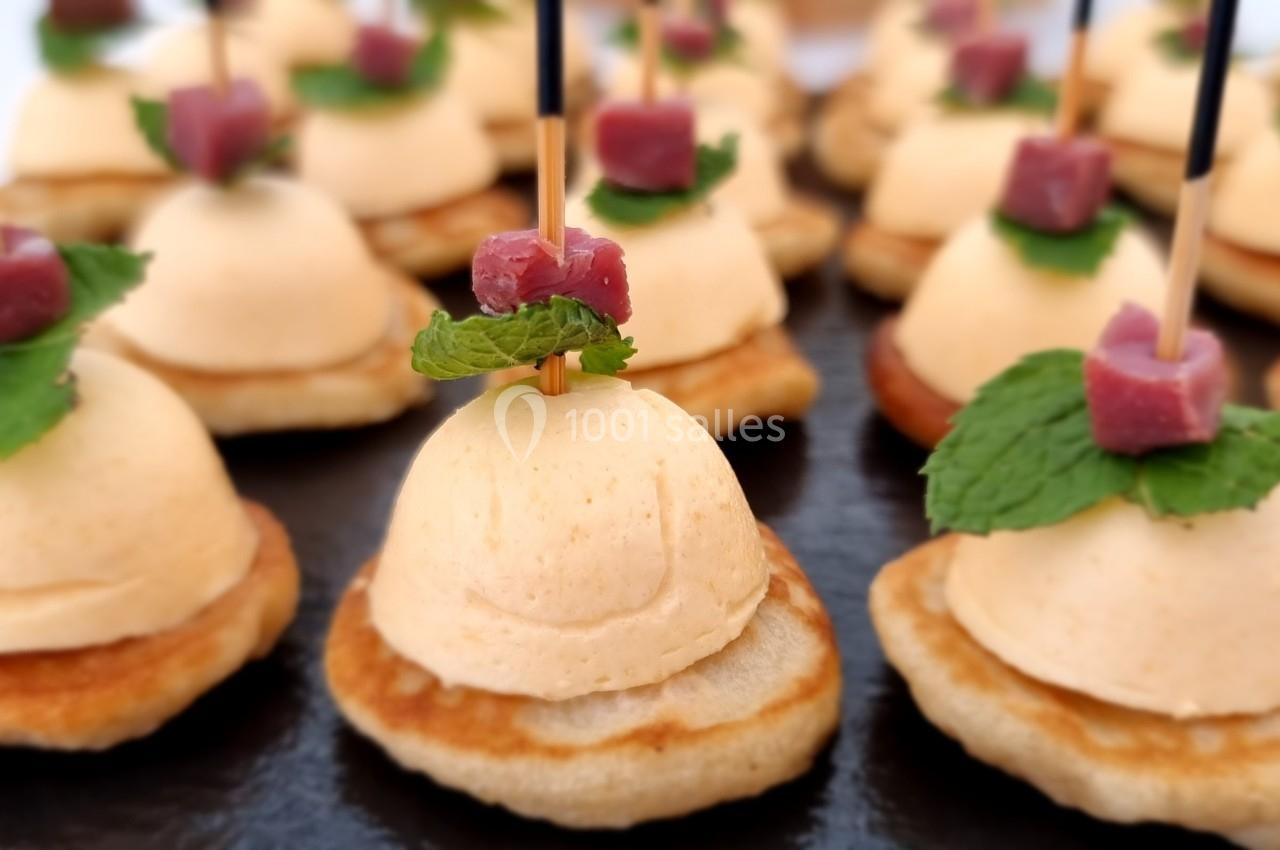 Bouchées apéritives composées de blinis, mousse, dés de viande et feuilles de menthe, présentées sur un plateau.